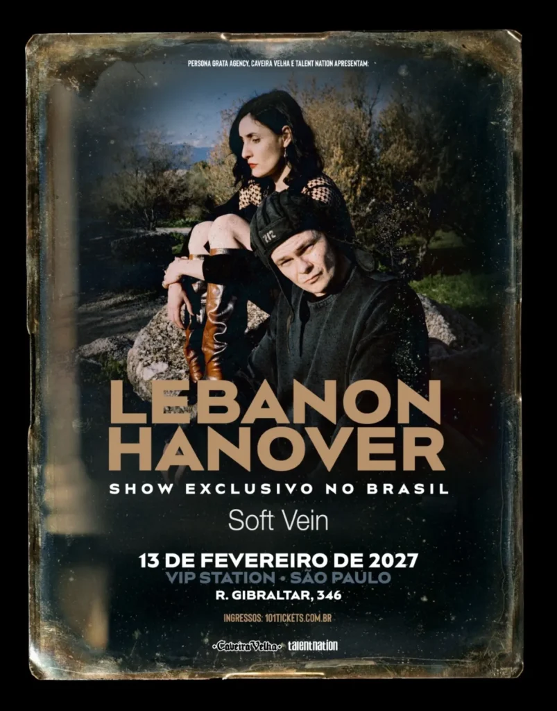 Cartaz promocional do show da dupla de post-punk Lebanon Hanover em moldura desgastada de foto antiga. Na parte superior, a integrante Larissa Iceglass aparece sentada em uma pedra ao ar livre, vestindo roupa preta e botas de couro marrom, enquanto William Maybelline está em primeiro plano usando uma touca de aviador escura com o número "712". No centro, destaca-se o nome "LEBANON HANOVER" em letras beges sobre a frase "SHOW EXCLUSIVO NO BRASIL" e a atração de abertura "Soft Vein". Na parte inferior, são anunciados a data e o local: 13 de fevereiro de 2027 na VIP Station (Rua Gibraltar, 346 - São Paulo), com ingressos pela 101tickets.com.br e realização de Persona Grata Agency, Caveira Velha e Talent Nation.